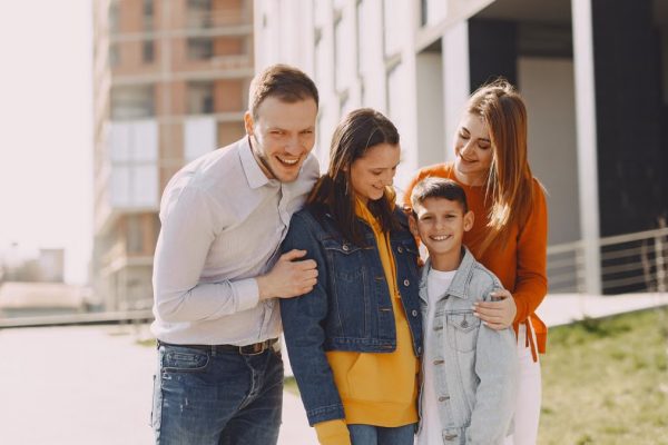 Delighted family in trendy casual wear holding each other and standing near modern building on city street while walking together during weekend